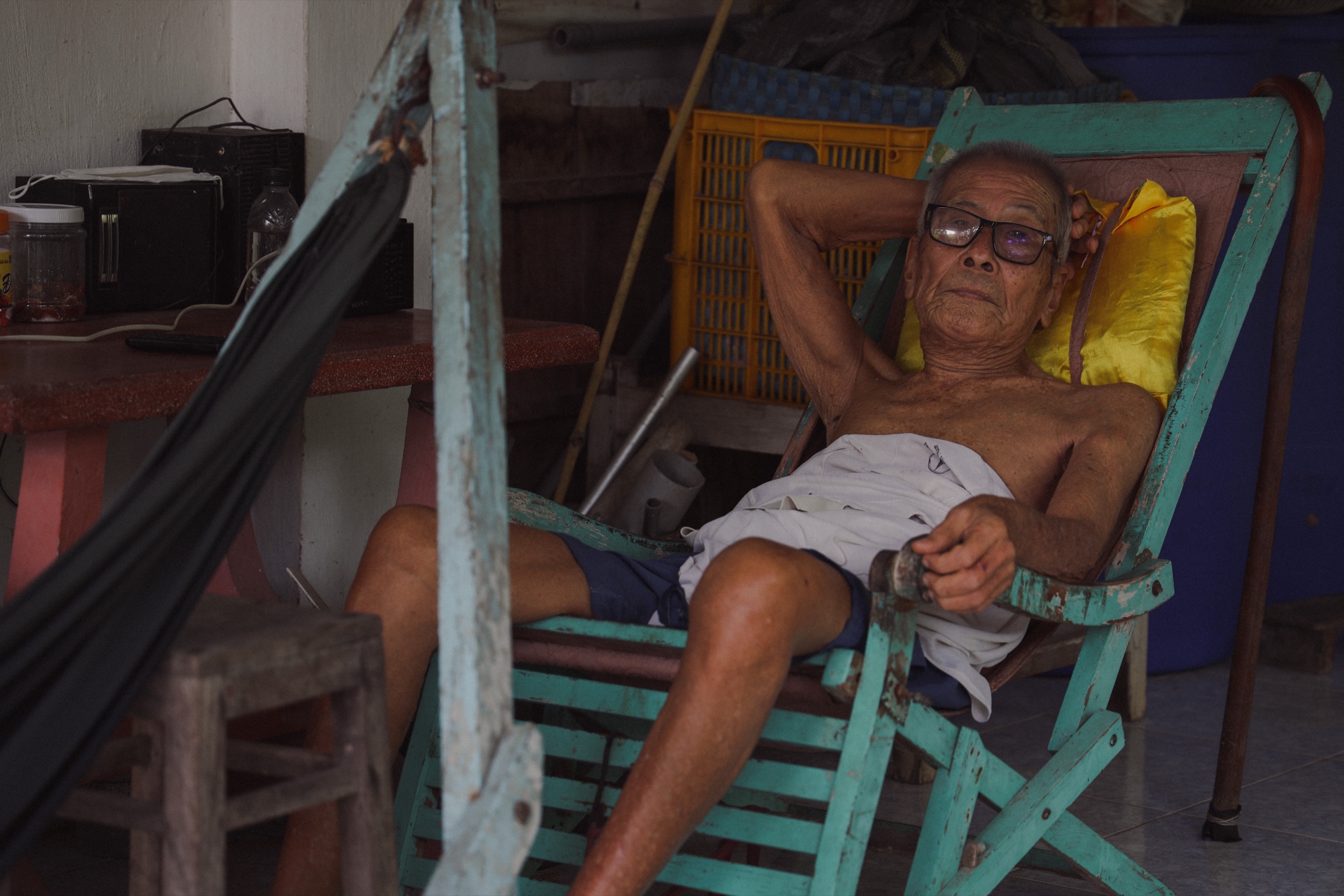 Grandfather reclining in a turquoise deck chair, one arm behind his head, looking at the camera.