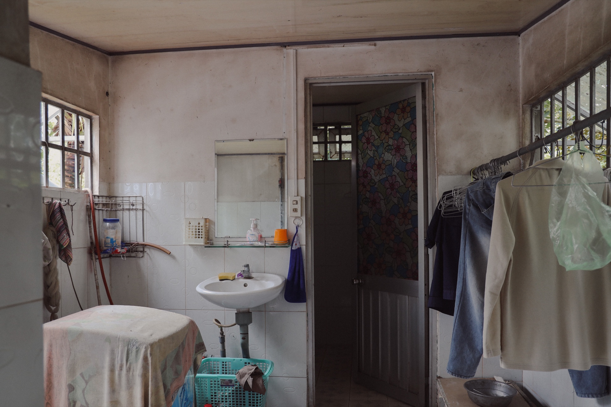 The washroom: a sink, a mirror, clothes on hangers, and a doorway through to a second door.