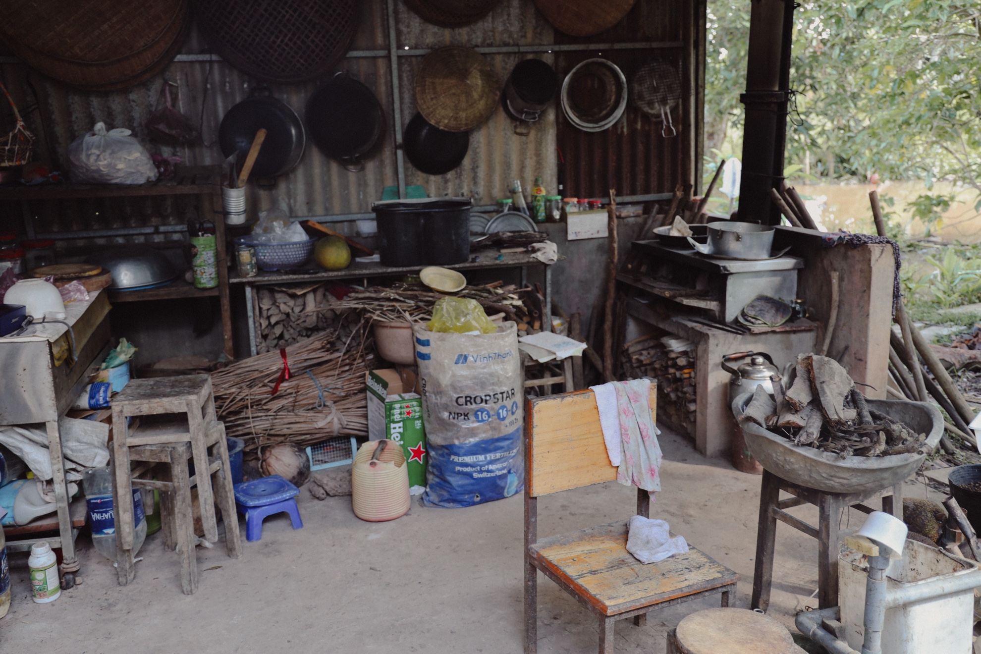 The outdoor kitchen: woks and baskets hung on corrugated tin, a wood stove, a chair with a towel.