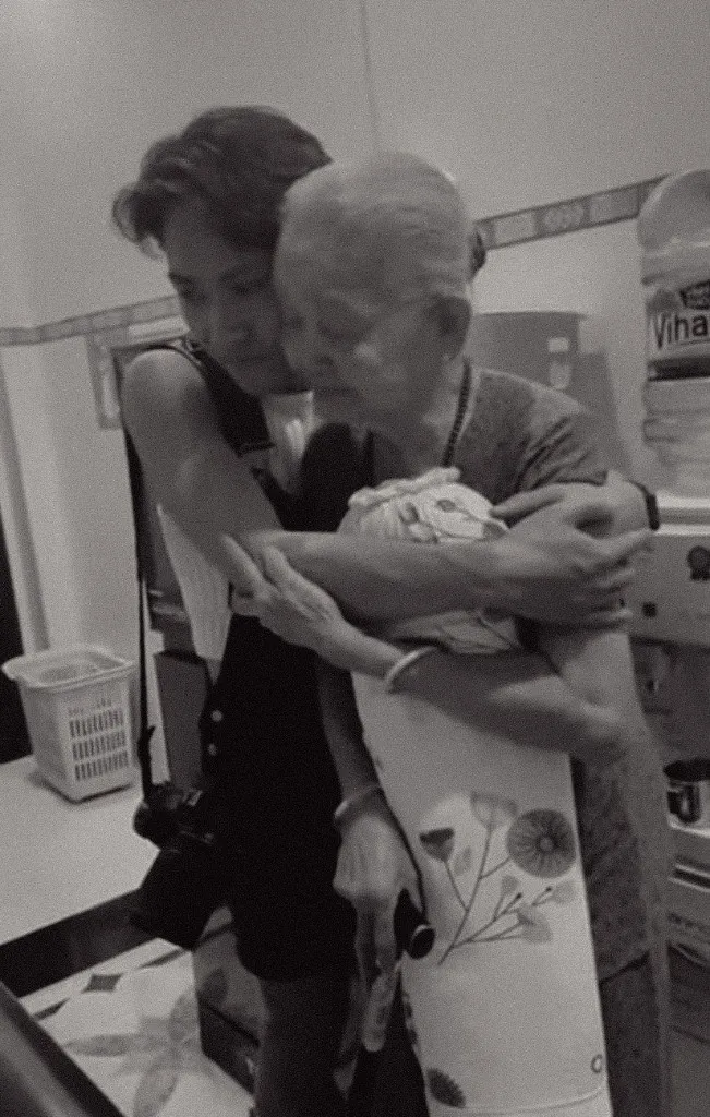 Grandmother held in an embrace at the bedroom door, still holding her pillow.