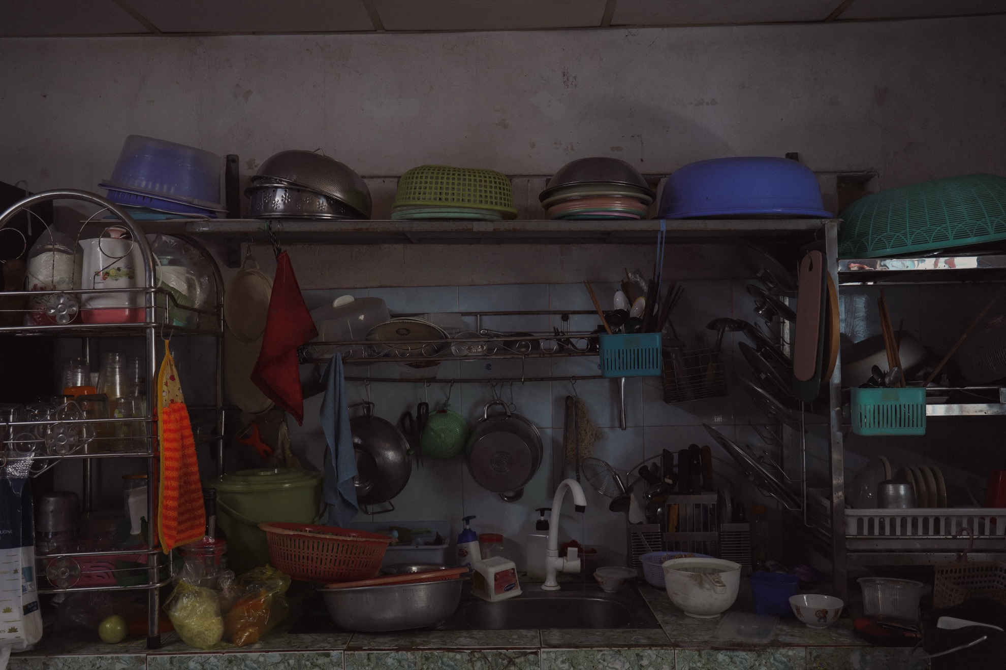 The kitchen wall: plastic bowls and steel pots on a rack above the sink.