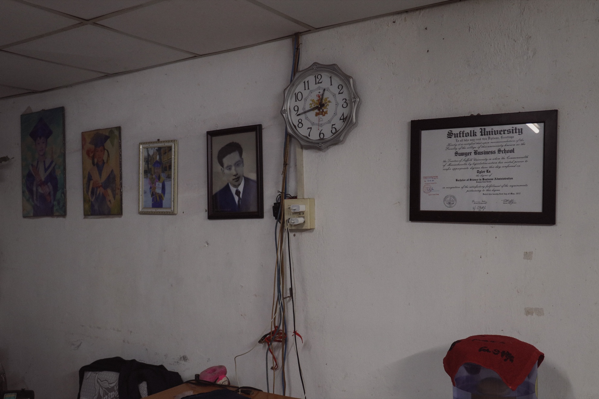 The living-room wall: family portraits, a clock, and a framed diploma.